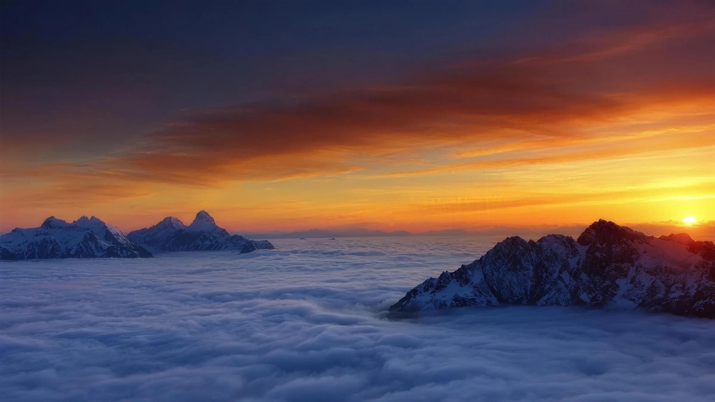Snow capped mountain peaks rising through a sea of clouds at sunset