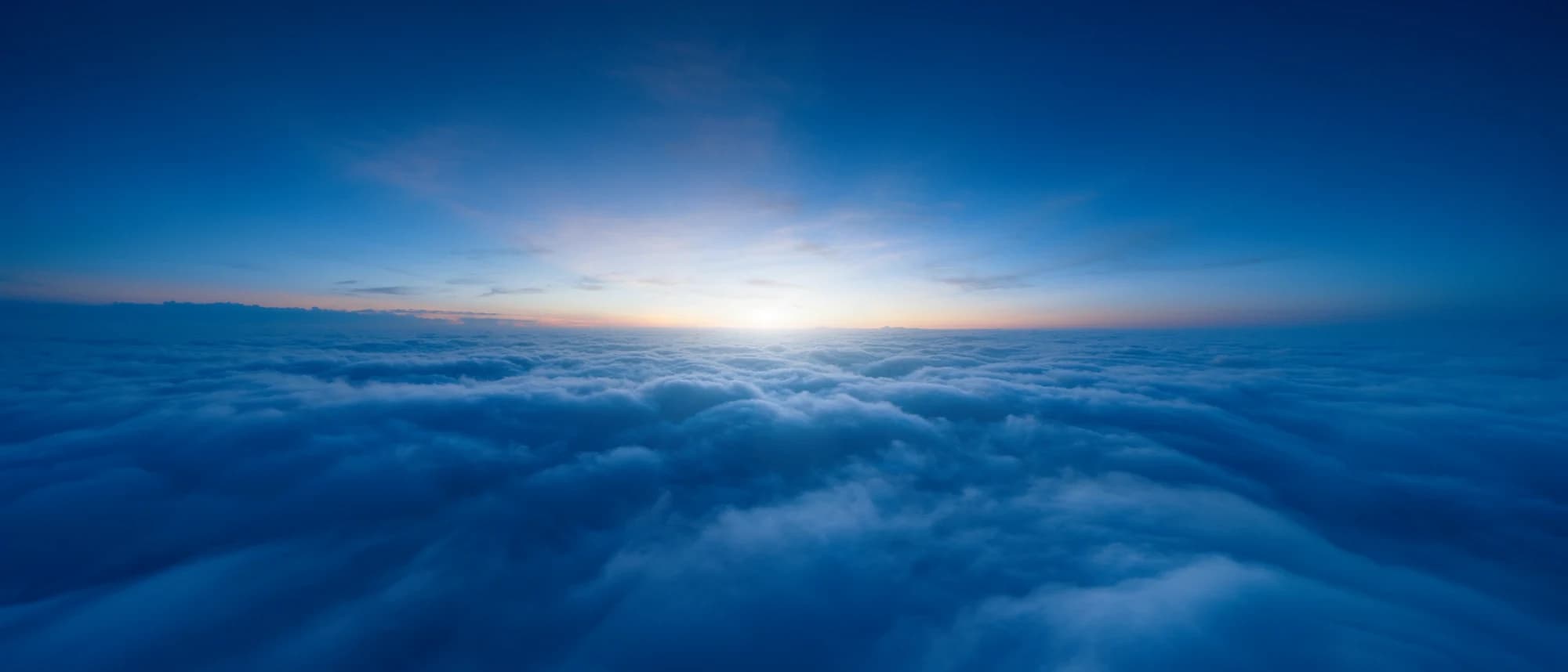A luminous sea of clouds at blue hour with a warm sunrise glow on the horizon