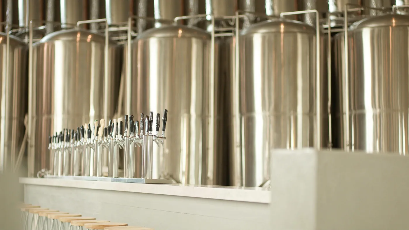 A modern brewery taproom with gleaming tanks behind a clean bar of taps